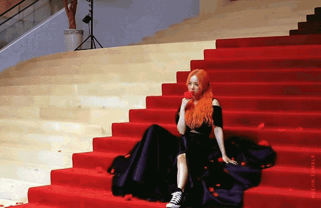 a woman sits on a set of red stairs holding a red rose