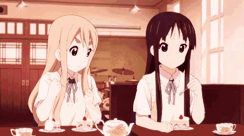 two anime girls sitting at a table eating cake