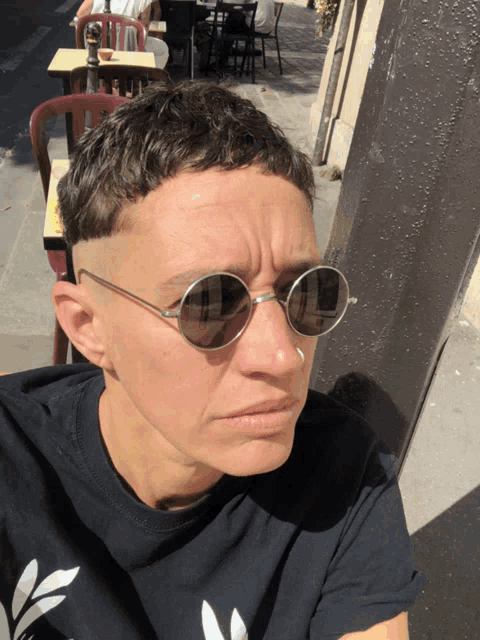 a woman wearing round sunglasses and a black shirt with a white leaf on it