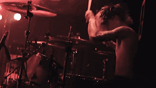 a man playing drums in a dark room with a red light behind him