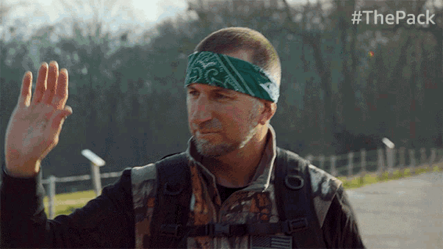 a man wearing a green bandana and a backpack is waving his hand