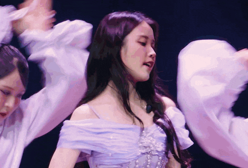 a woman in a purple off the shoulder dress is dancing on stage