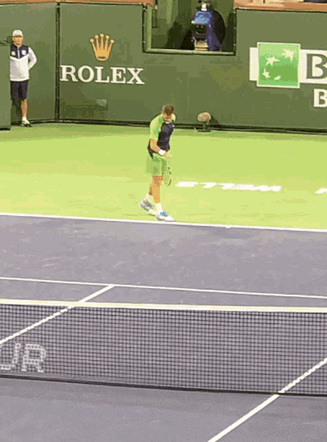 a tennis player stands on a tennis court in front of a rolex banner