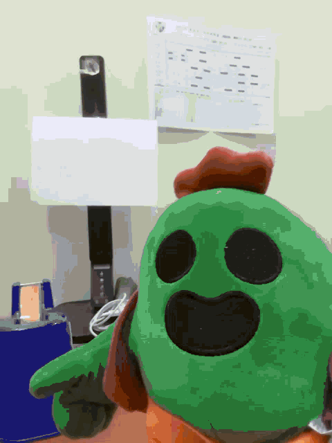a green stuffed animal with black eyes and a red hat