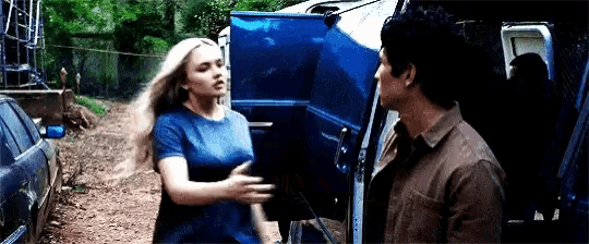 a man and a woman are standing next to each other in front of a car with the door open .