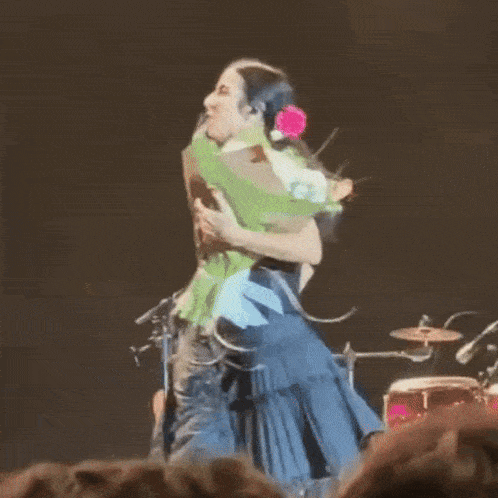 a man is carrying a woman on his shoulders on a stage while she holds a bouquet of flowers .