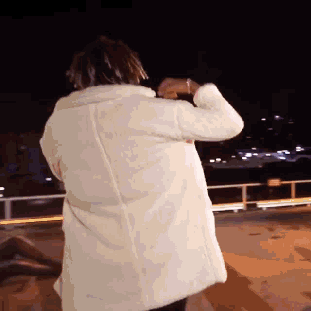 a woman in a white coat is standing in front of a bridge at night