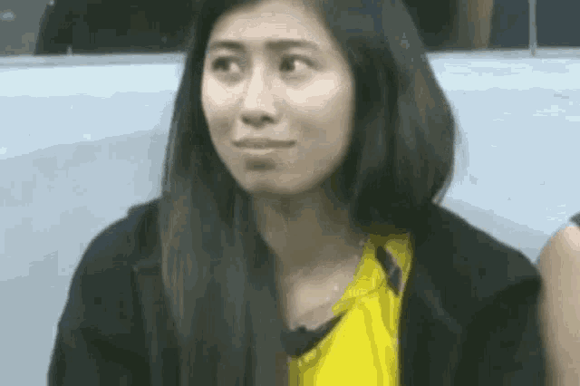 a close up of a woman wearing a yellow shirt and a black jacket making a funny face .