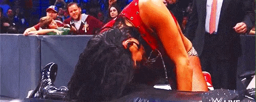 a female wrestler is laying on the ground during a wrestling match while a crowd watches .