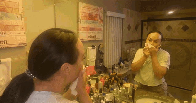 a woman wipes her face in front of a mirror with a sign behind her that says ' s.p. '