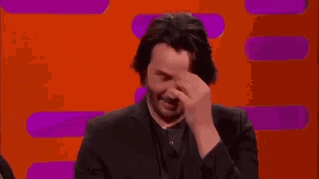 a man in a suit is sitting in front of an orange and purple background with the word wow written in green .