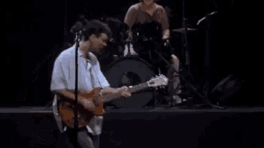 a man is playing a guitar on a stage in front of a drummer .