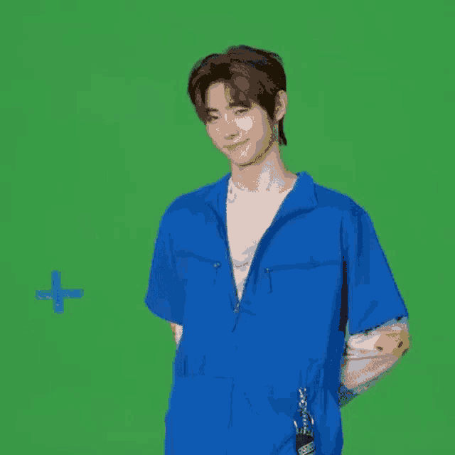 a young man in a blue jumpsuit is standing in front of a green background .