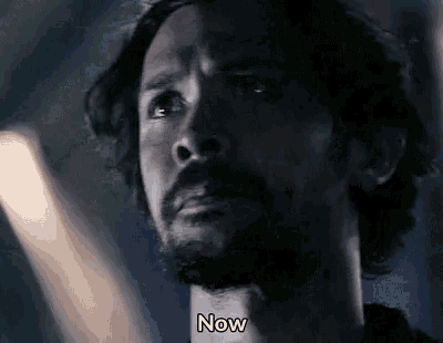 a man with a beard is looking at the camera with the words `` now '' written below him .