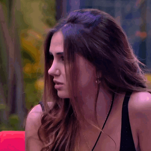 a woman wearing a black tank top and a necklace looks at the camera with her eyes closed