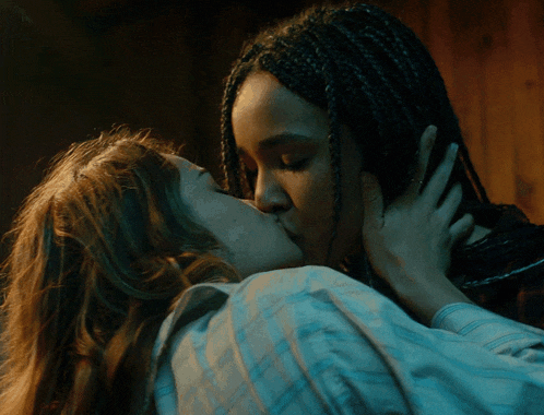 a woman with braids is kissing another woman in a blue shirt