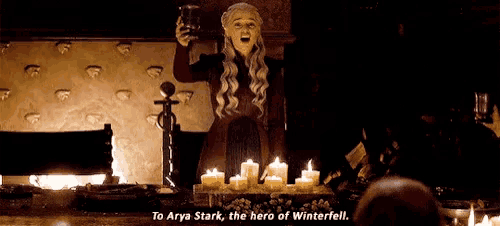 a woman is holding a cup in front of candles and says to arya stark , the hero of winterfell