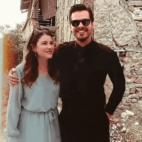 a man and a woman are posing for a picture in front of a stone wall
