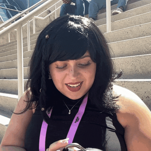 a woman wearing a black top with a purple lanyard around her neck that has the letter s on it