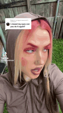 a woman with pink hair is wearing a hoodie and a piercing in her nose .