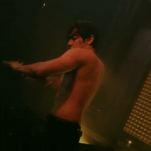 a shirtless man is kneeling down in a dark room with his arms outstretched .