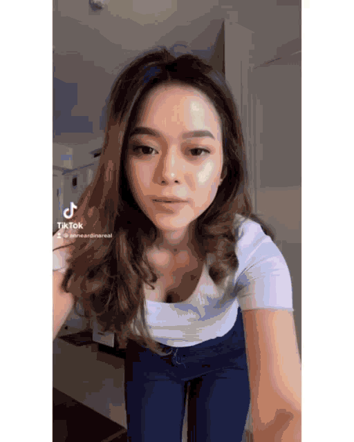 a woman in a white shirt and blue jeans is standing in front of a mirror .