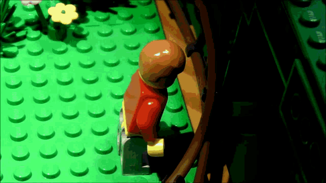 a lego figure stands on a green surface with a flower in the background
