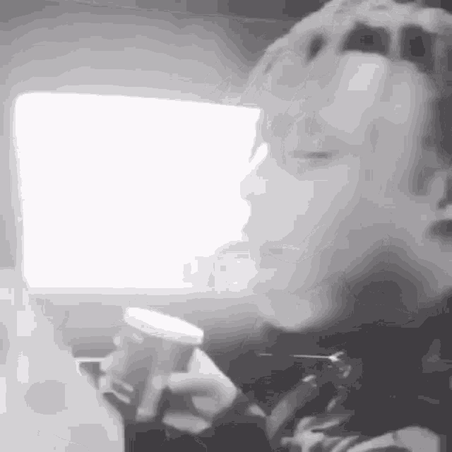 a black and white photo of a person in a car drinking from a cup .