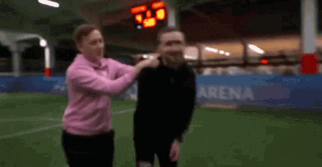 a man in a pink shirt is putting his hand on another man 's neck on a soccer field .