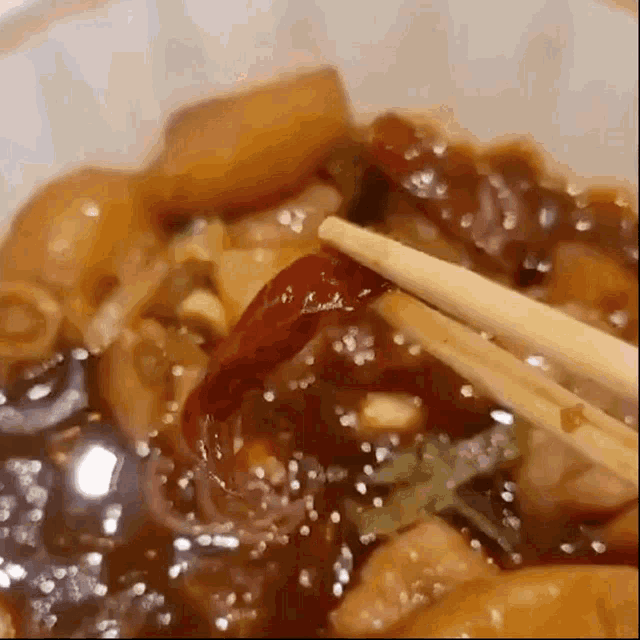 a close up of chopsticks holding a red pepper in a bowl of food .
