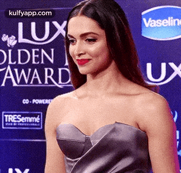 a woman in a strapless dress is standing on a red carpet in front of a vaseline sign .