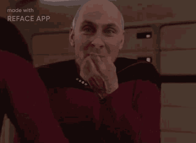 a bald man in a red jacket is covering his mouth with his hands .