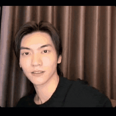 a young man in a black shirt is looking at the camera .
