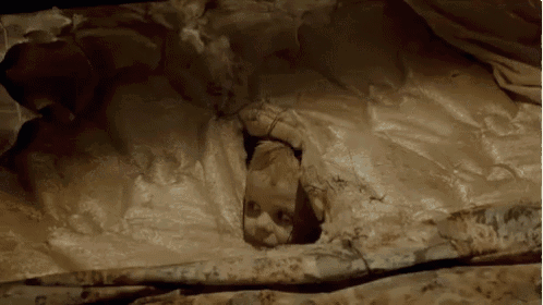 a baby is sticking its head out of a hole in a bedspread .