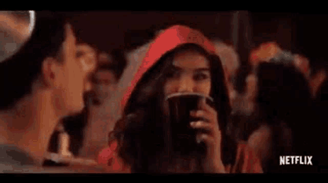 a woman in a red hood is holding a cup and talking to a man in a devil costume .