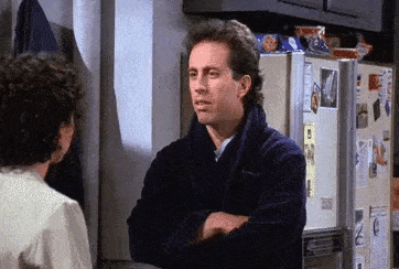 a man in a robe is standing in front of a refrigerator and talking to a woman .