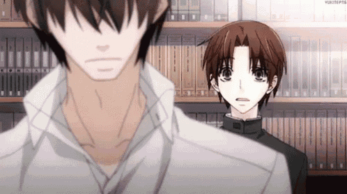 a couple of anime characters standing next to each other in front of a bookshelf .