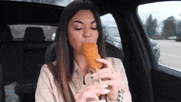 a woman is sitting in a car eating a fried food stick