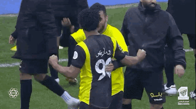 a group of soccer players are hugging each other on a field . one of the players has the number 99 on his jersey .
