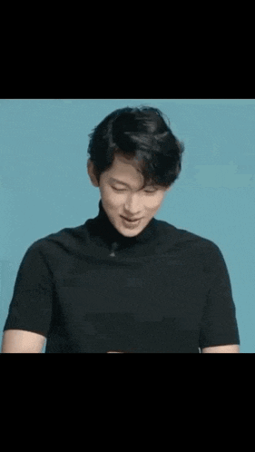 a young man wearing a black turtleneck is smiling against a blue background .