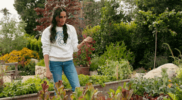 a woman wearing a sweatshirt that says university is standing in a garden with lots of plants