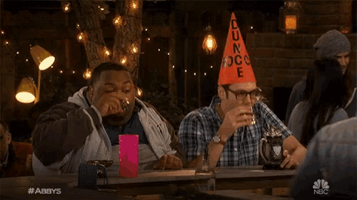 two men sitting at a table with one wearing an orange cone that says dun rock