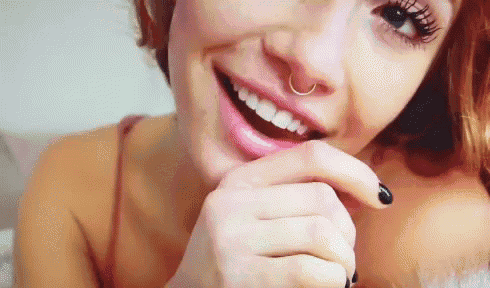 a close up of a woman 's face with a nose ring and black nails