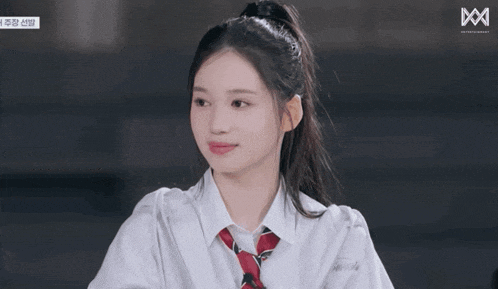 a girl with her eyes closed is wearing a white shirt and a red tie with the letter m on the bottom