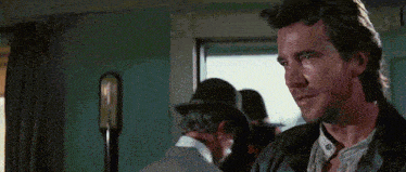 a man in a leather jacket is standing in front of a window in a room .