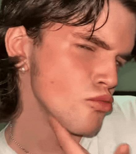 a close up of a young man 's face with his hand on his chin making a funny face .