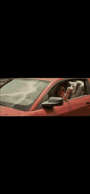 a woman in sunglasses is driving a red car
