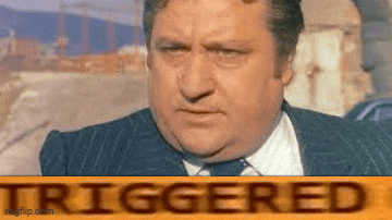 a man in a suit and tie is sitting in front of a sign that says triggered .