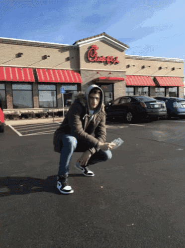 a man is squatting in front of a chick-fil-a restaurant