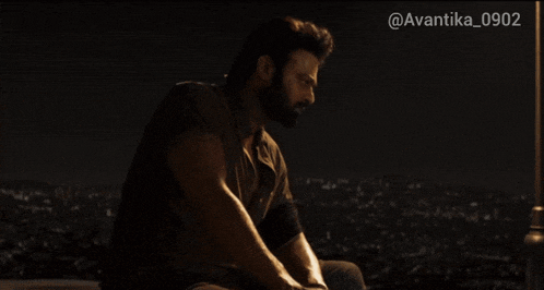 a man with a beard sits on a ledge with a city in the background and the hashtag avantika_0902